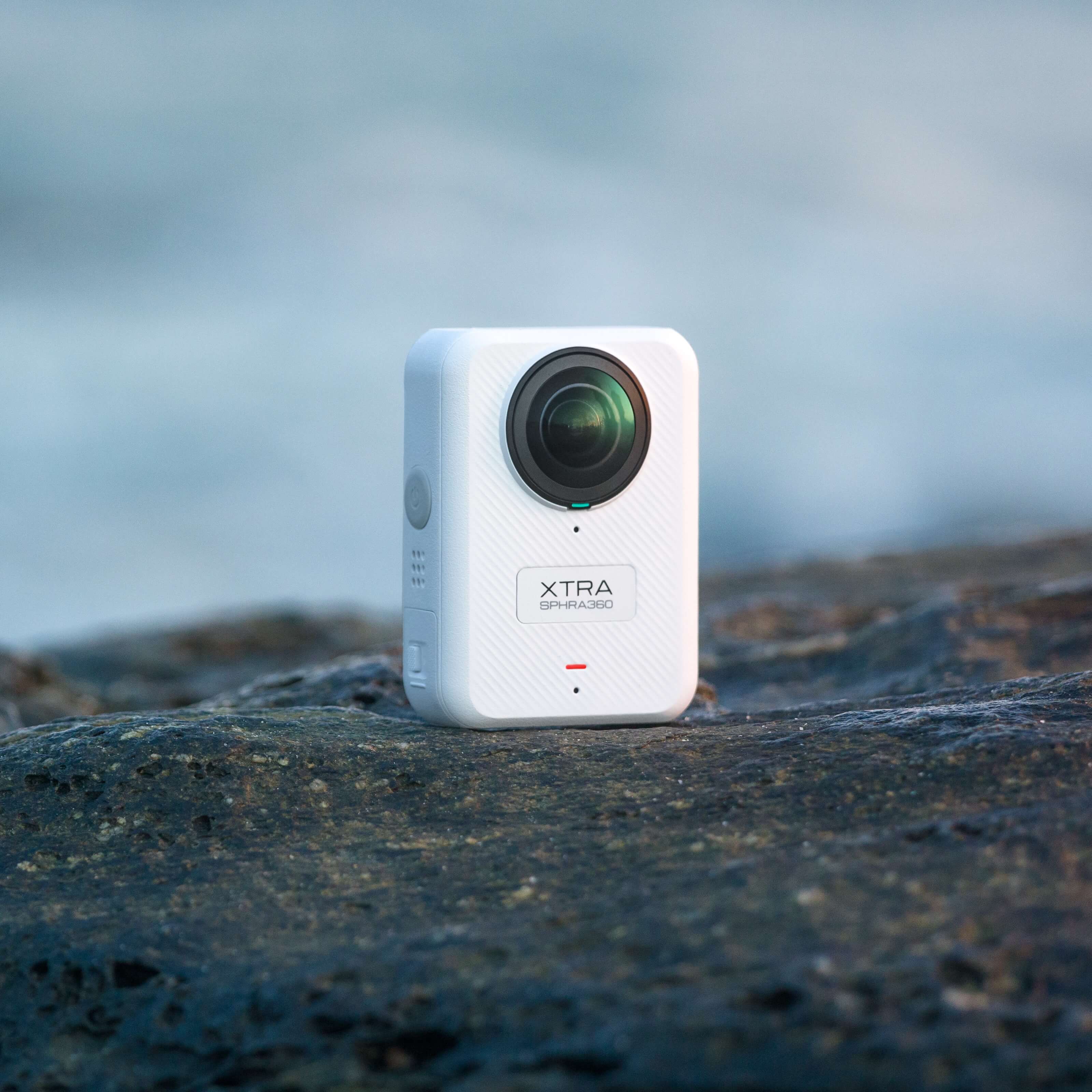 White Xtra Sphra360 8K action camera placed on rugged rocky terrain for outdoor shooting.